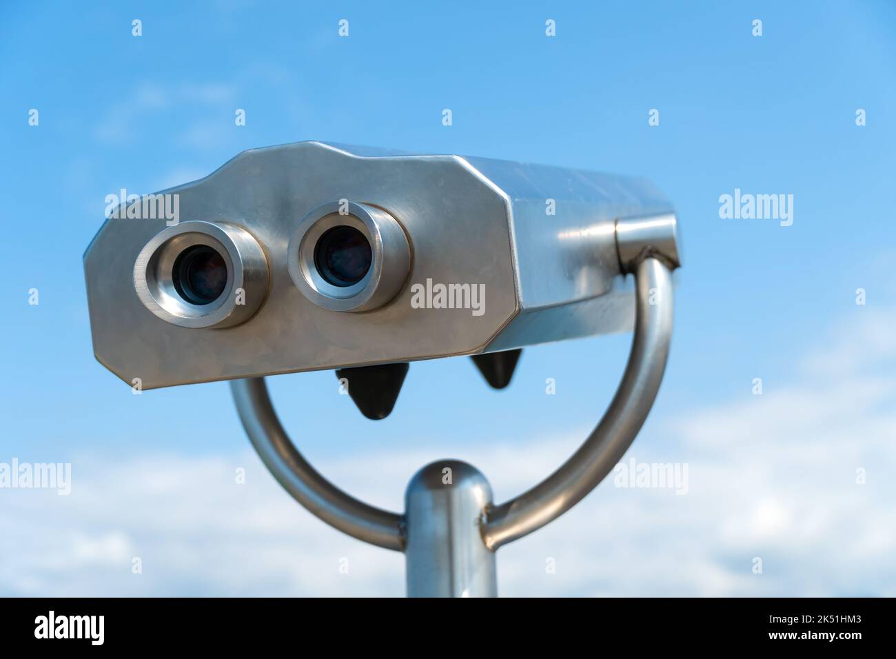 Gros plan d'une paire de jumelles fixes gris en métal sur le pont d'observation contre le ciel bleu par une journée ensoleillée. Bizarre homme de métal imaginaire Banque D'Images