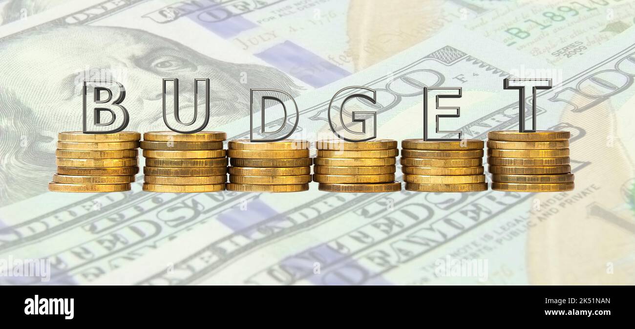 Le mot « Budget » fait de lettres de verre, se tenant sur des piles de pièces de monnaie sur le fond de billets en dollars. Le concept d'un budget propre. Banque D'Images