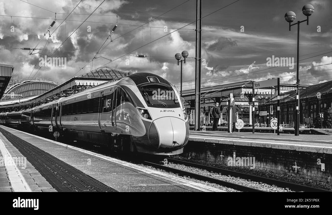 Un train s'arrête à une plate-forme de gare. Deux membres de l'équipage discutent et une locomotive est au premier plan. Un ciel avec le nuage est au-dessus. Banque D'Images