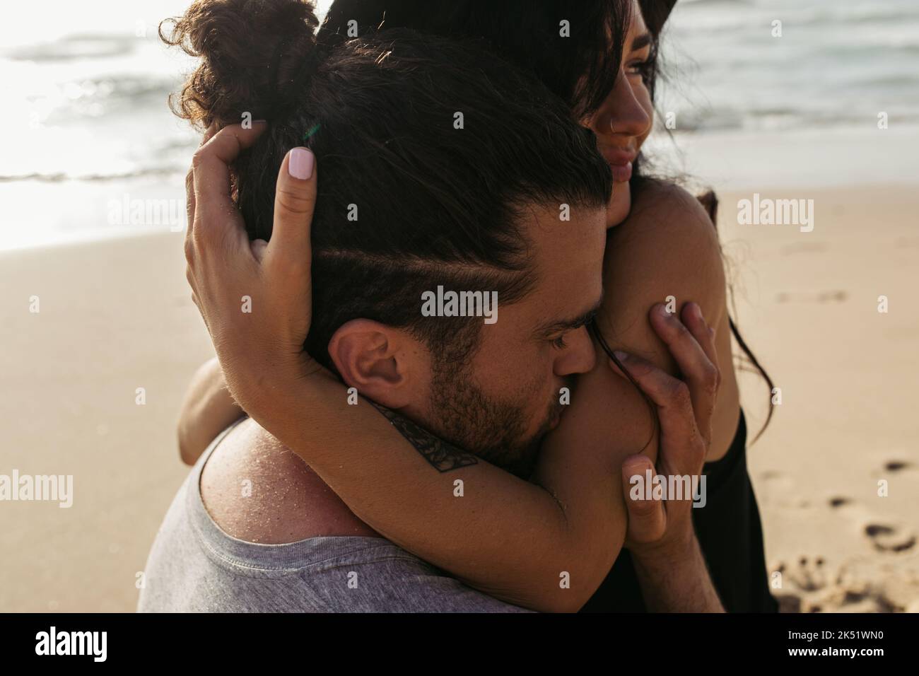 homme barbu embrassant la main sur la femme heureuse avec tatouage sur la plage, image de stock Banque D'Images