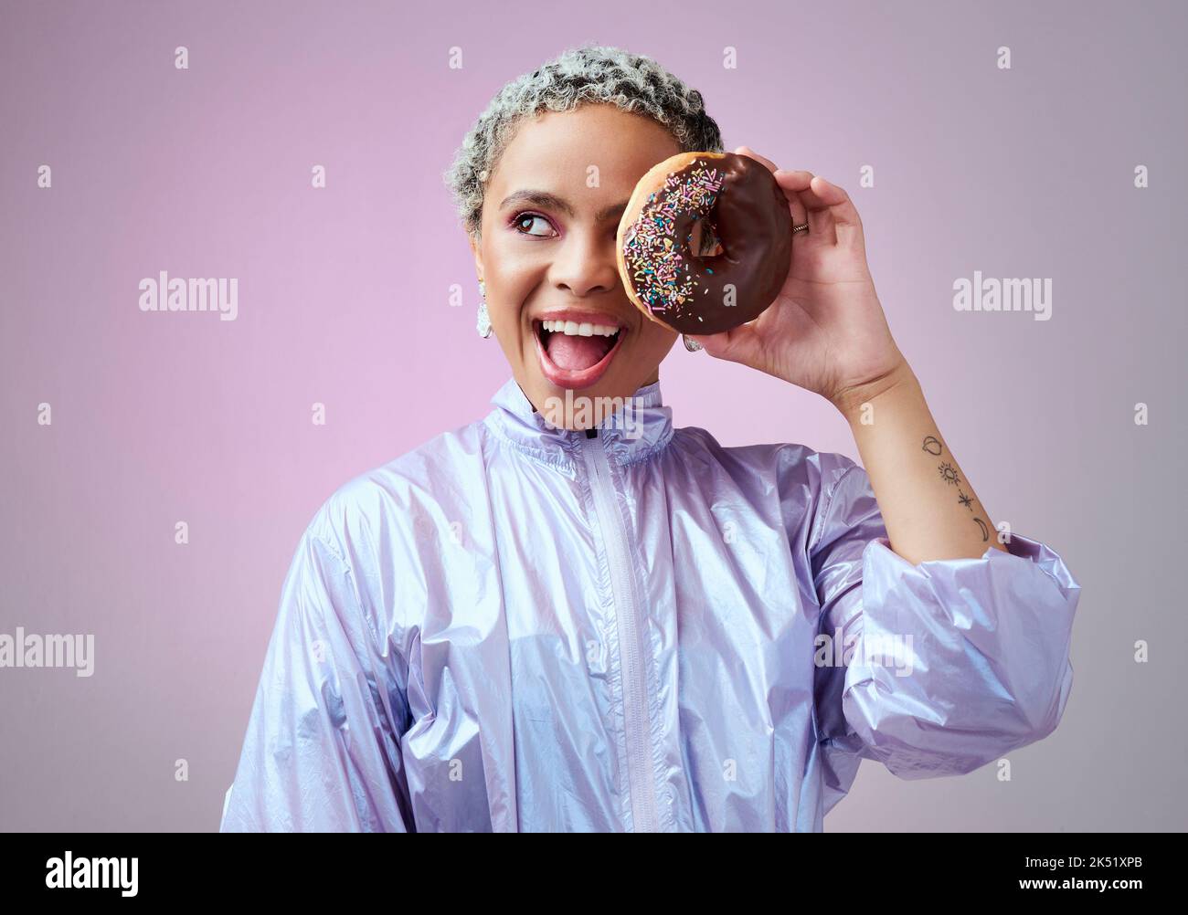 Mode, donut et femme noire excitée et heureuse au sujet du dessert avec des vêtements futuristes de style vaporwave ou holographique sur fond violet. Face Banque D'Images