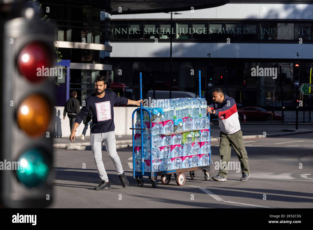 Les travailleurs manœuvrent un chariot transportant un grand nombre de bouteilles d'eau minérale par temps chaud à Londres, en Angleterre, au Royaume-Uni Banque D'Images