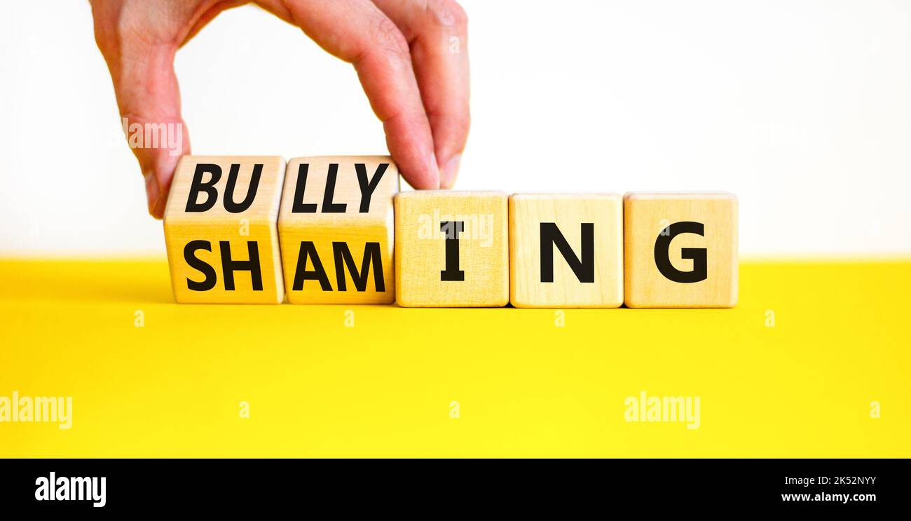 Symbole de honte et d'intimidation. Concept mots Shaming et Bulbing sur des cubes en bois. Main d'homme d'affaires. Magnifique table jaune fond blanc. Affaires s Banque D'Images