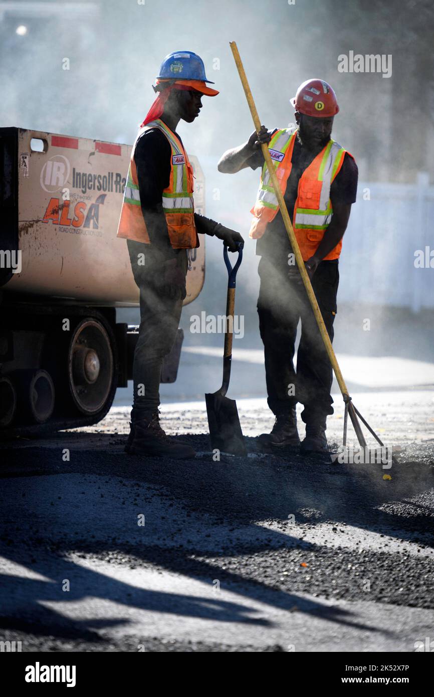 Une équipe de pavage de routes ou de rues travaillant à réparer une surface d'asphalte à l'aide de râteaux et de pelles Banque D'Images