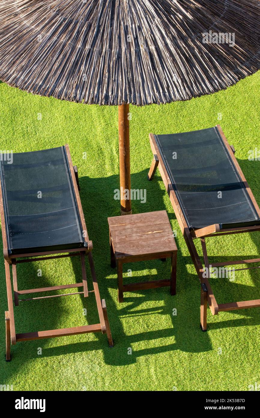 deux chaises longues ou chaises longues avec un parasol en bambou sur la fausse herbe dans une villa sur l'île grecque de zante ou zakynthos, vacances au soleil, chaises longues. Banque D'Images