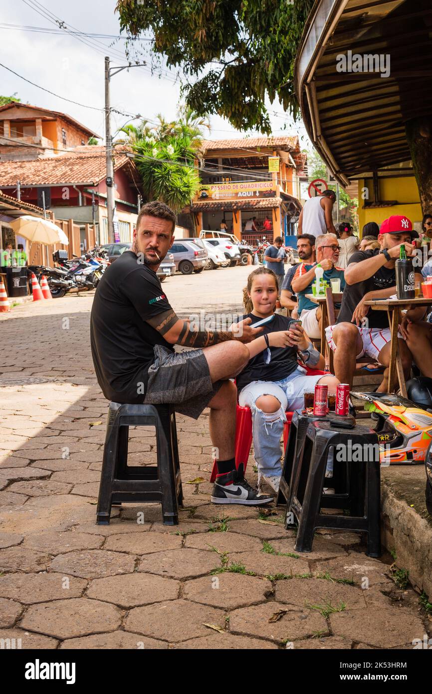 Homme et fille assis sur des bancs dans la rue principale en face d'un restaurant à São Sebastião das Águas Claras, Macacos, Minas Gerais, Brésil. Banque D'Images