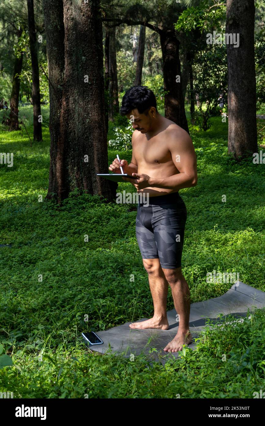 Des yogi masculins actifs et beaux se promène dans un parc en forêt avant ou après un entraînement. Un jeune athlète hispanique d'homme d'athlétisme va à la classe de yoga avec un fi Banque D'Images