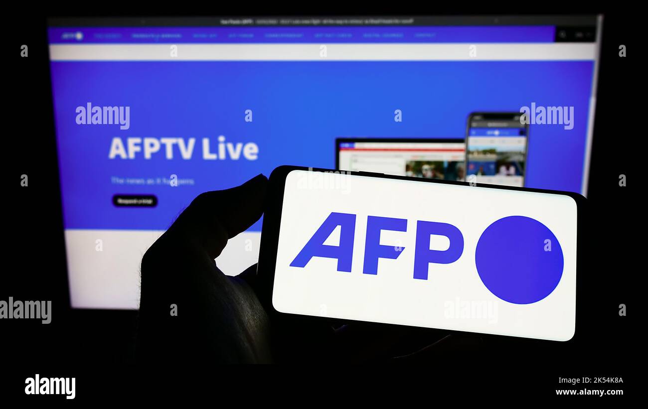 Personne tenant un téléphone portable avec logo de l'agence de presse Agence France-presse (AFP) sur écran en face de la page web d'affaires. Mise au point sur l'affichage du téléphone. Banque D'Images