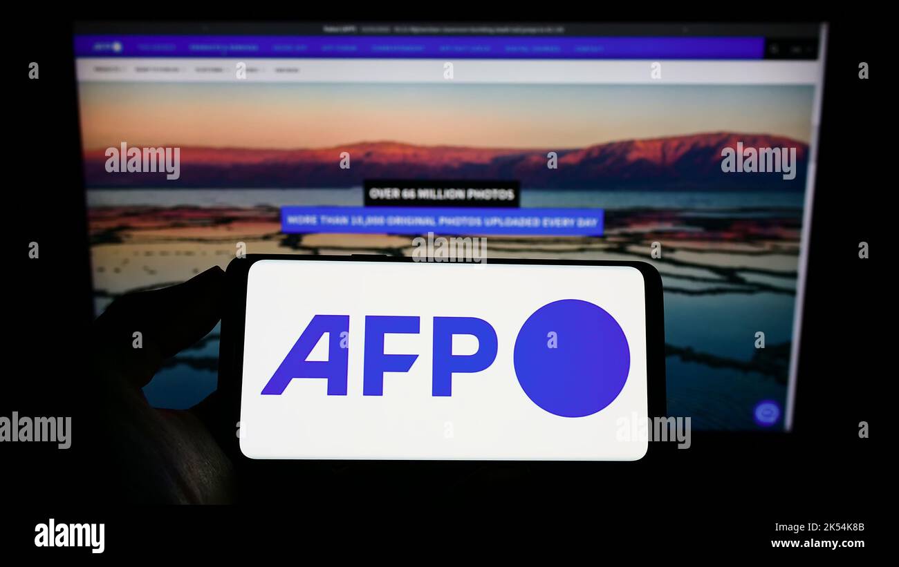 Personne tenant un téléphone portable avec logo de l'agence de presse Agence France-presse (AFP) à l'écran en face de la page web d'affaires. Mise au point sur l'affichage du téléphone. Banque D'Images