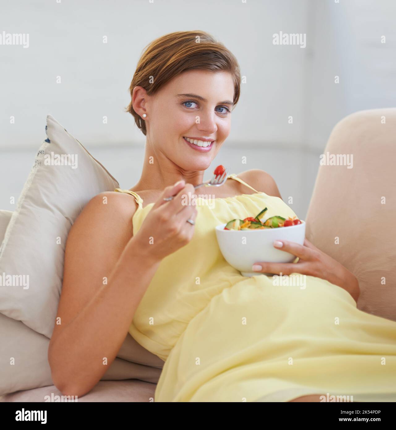 Mon bébé aime la salade autant que moi. Une belle femme enceinte se détendant sur le canapé tout en mangeant une salade fraîche. Banque D'Images