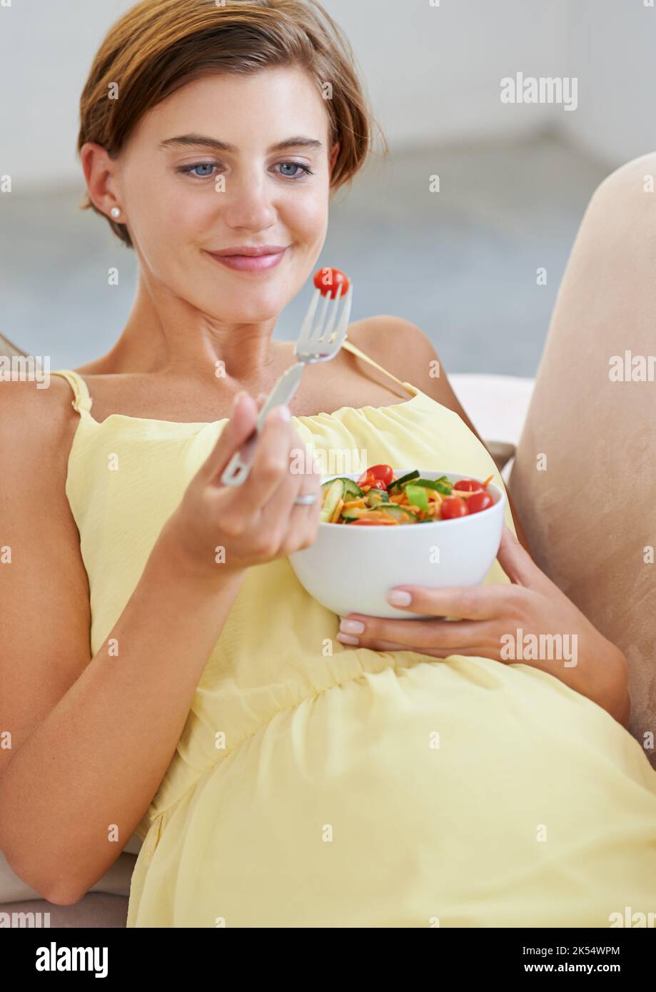 Des débuts sains une belle femme enceinte se détendant sur le canapé tout en mangeant une salade fraîche. Banque D'Images
