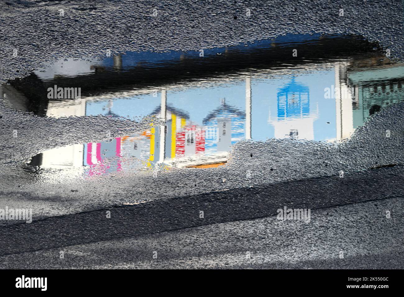 Les peintures murales du bord de mer des cabanes de plage et du phare se reflètent sur la route humide de Mumbles Pier après que la pluie ait disparu. Banque D'Images