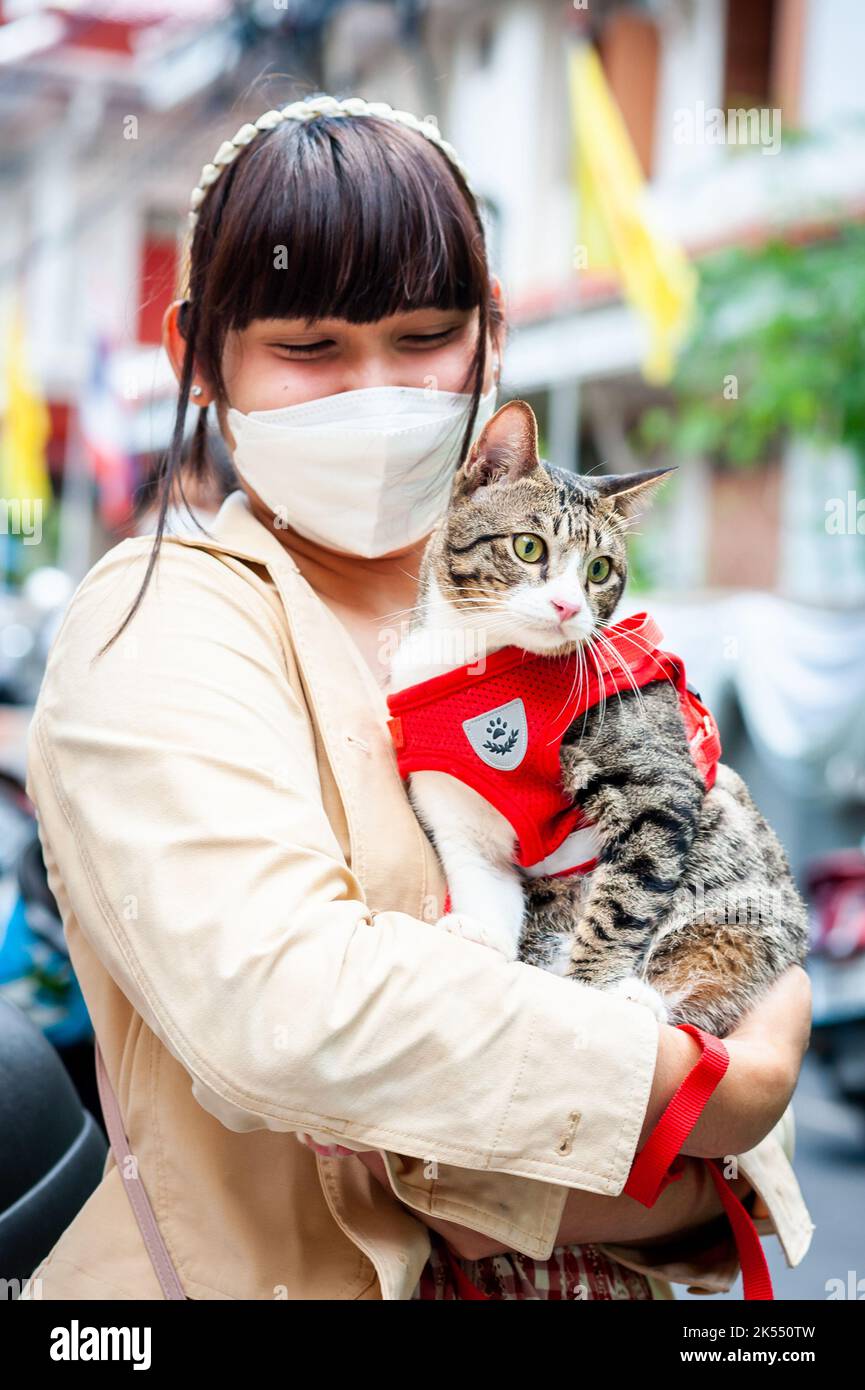 Une jeune femme thaïlandaise tient son beau chat portant une petite veste rouge à l'extérieur du temple Wat Paknam Phasi Chaloen, Bangkok, Thaïlande. Banque D'Images