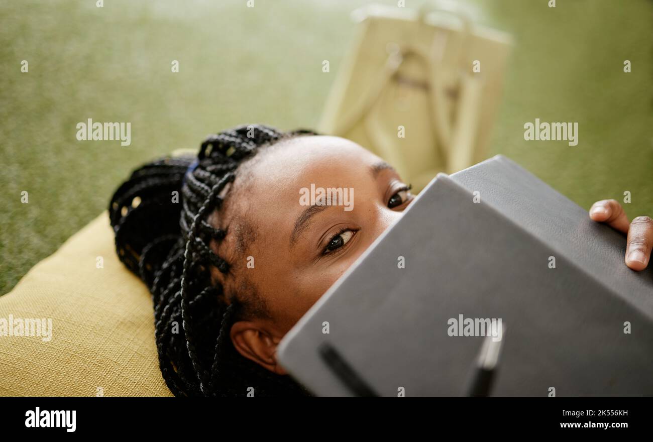 Une femme noire et un étudiant se cachent face avec un carnet sur un petit sac de haricot. Timide apprenant universitaire africain sur l'étude de pause repos Banque D'Images