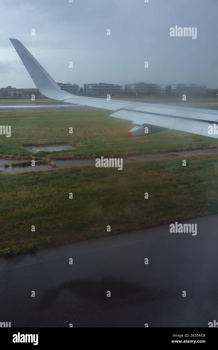 Vue à travers une fenêtre d'avion à avec la pluie traversant le portail, à la vue de la piste et jour humide dehors. Banque D'Images