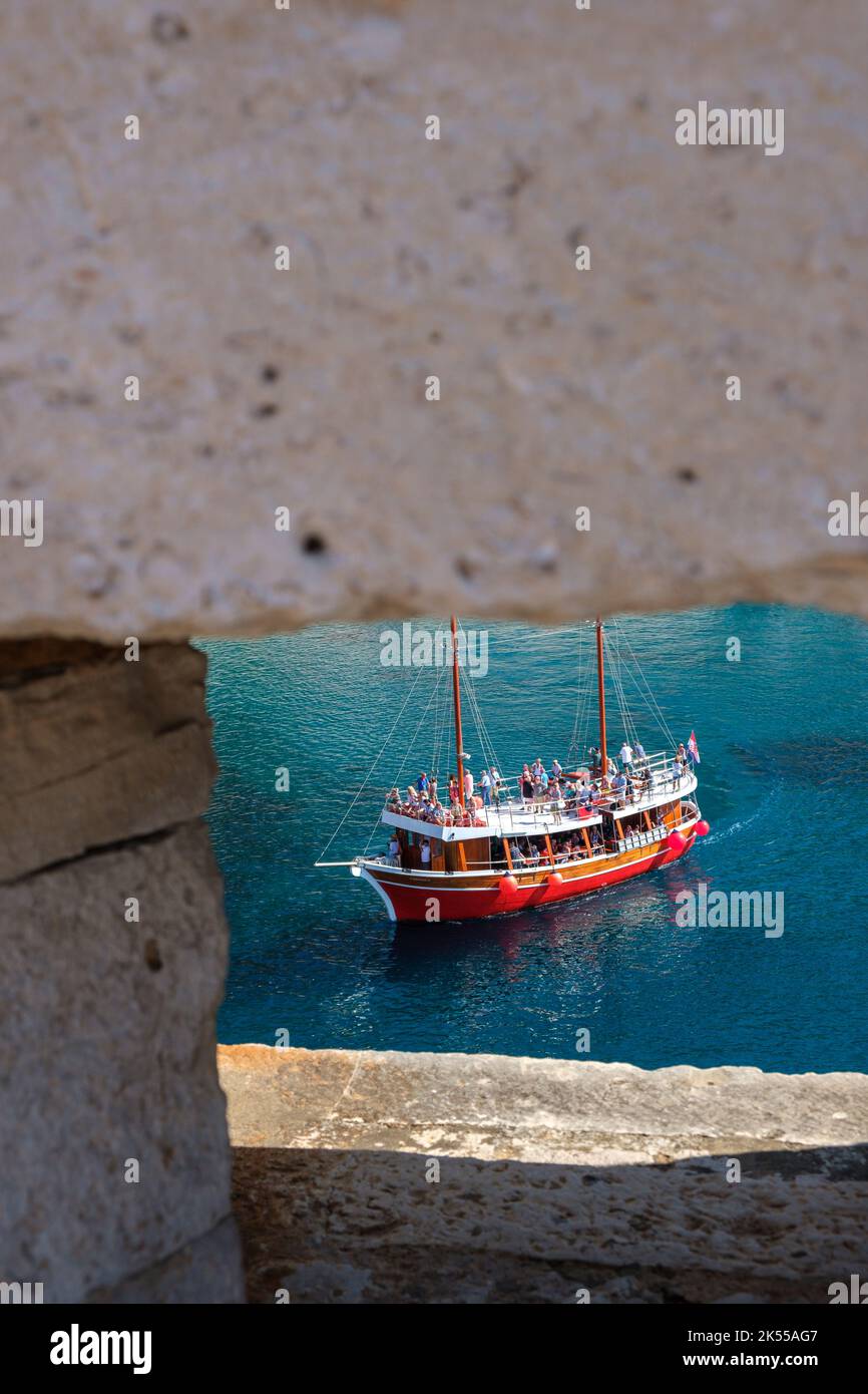 Un petit bateau transportant des touristes dans le port de la vieille ville de Dubrovnik vu à travers un vide dans les murs de la ville. Banque D'Images