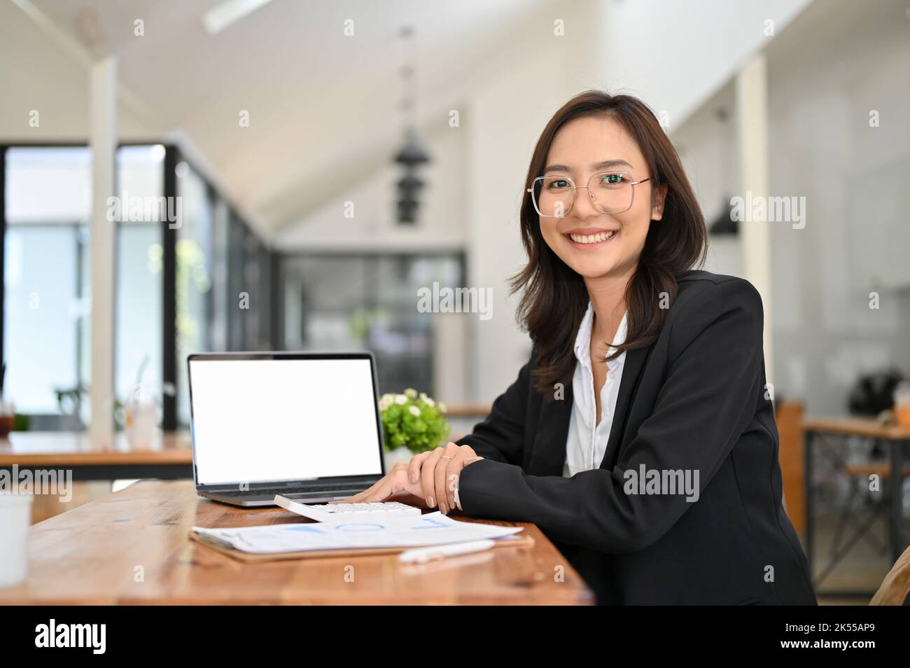 Une femme d'affaires ou une comptable asiatique du millénaire, attirante et professionnelle, portant des lunettes, est assise à son bureau avec un écran vierge d'ordinateur portable Banque D'Images