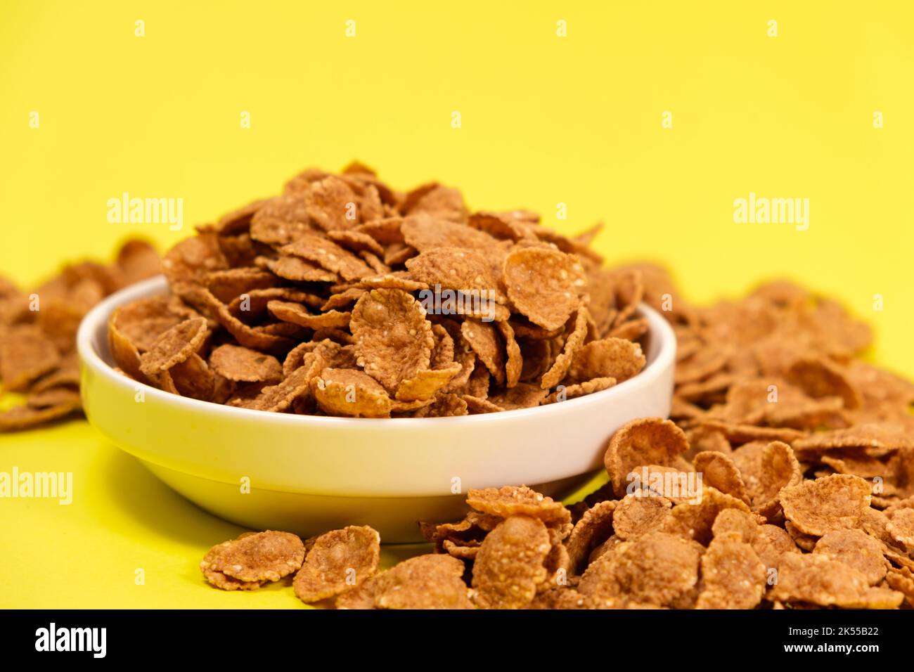 Flocons de blé dur - céréales pour petit déjeuner rapide sur une assiette sur fond jaune, espace pour le texte. Banque D'Images