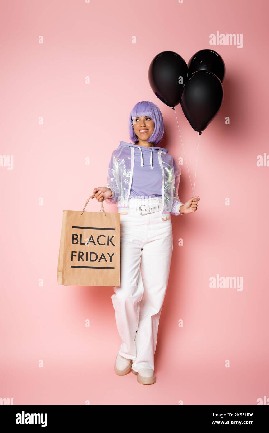 pleine longueur de bonne femme afro-américaine dans perruque violette tenant sac à shopping avec le lettrage du vendredi noir et ballons sur rose, image de stock Banque D'Images