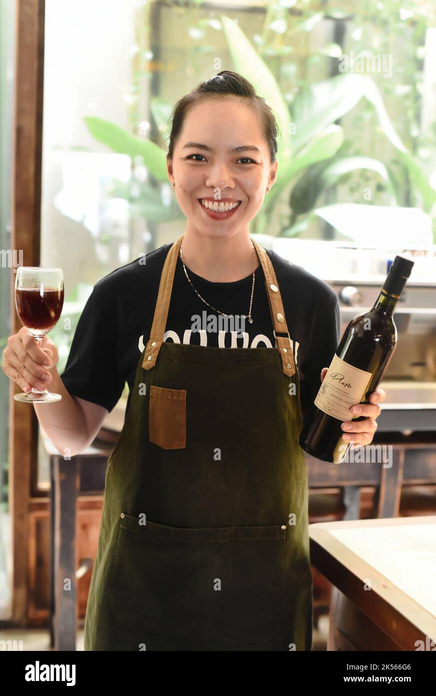 Bonne serveuse vietnamienne souriant et tenant une bouteille de vin de prune maison et un verre de vin Banque D'Images