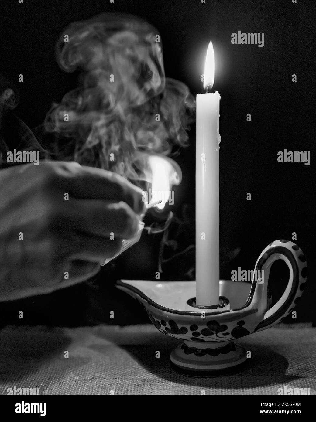 Une main tient un match éclairé après avoir allumé une bougie, avec un nuage de fumée dans le fond sombre Banque D'Images