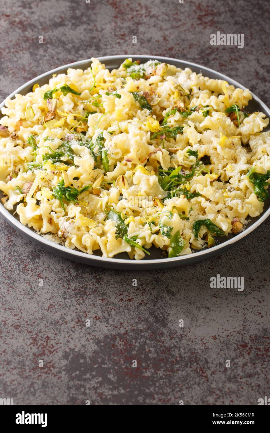 Mafalda pâtes à l'arugula, pistaches, parmesan et zeste de citron sur une assiette sur la table. Verticale Banque D'Images