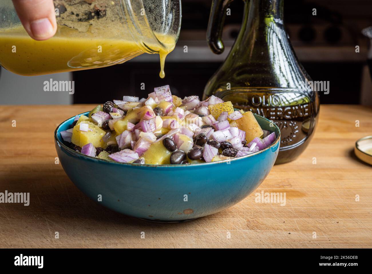 Salade d'oignons, de haricots et de pommes de terre dans un bol bleu avec vinaigrette jaune Banque D'Images