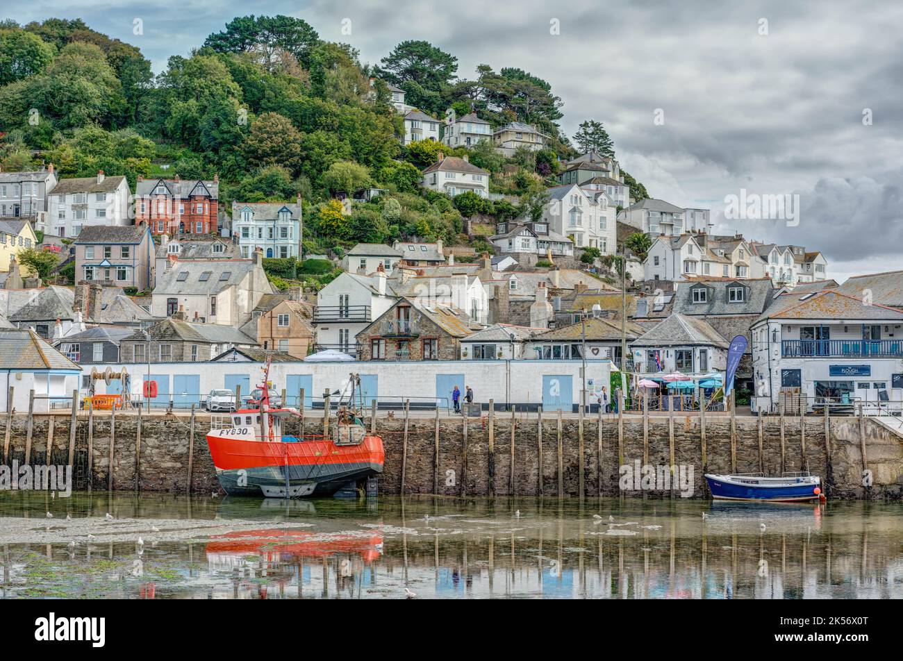 Une magnifique scène portuaire avec un bateau de pêche et un bateau à rames le long du long quai de Looe, en Cornouailles. Un jour gris nuageux et à marée basse. Banque D'Images