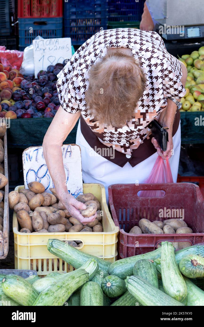 Une femme âgée est montrée triant et choisissant des pommes de terre sur un stand de légumes dans le Laiki, le marché populaire de rue à Rhodes ville, Rhodes Banque D'Images