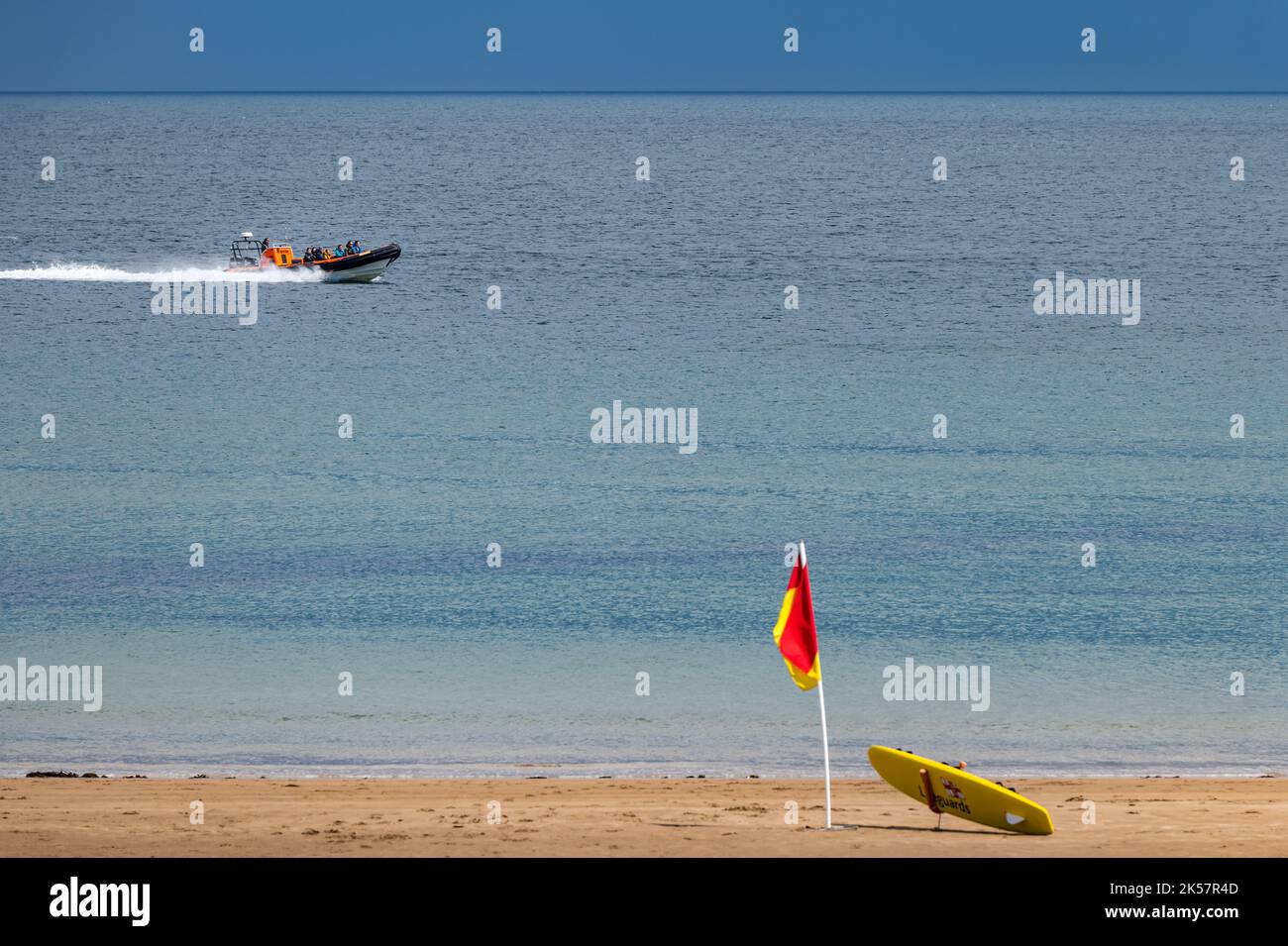 Touristes dans un bateau gonflable rigide en été, près de la plage avec le drapeau du maître-nageur Coldingham Bay, Berwickshire, Écosse, Royaume-Uni Banque D'Images