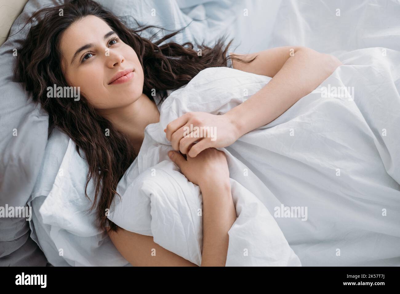 Une matinée agréable. Week-end loisirs. Accueil hygge. Beauté bien-être. Une femme de brunette pensive et détendue rêvant de dormir dans un lit blanc confortable souriant. Banque D'Images