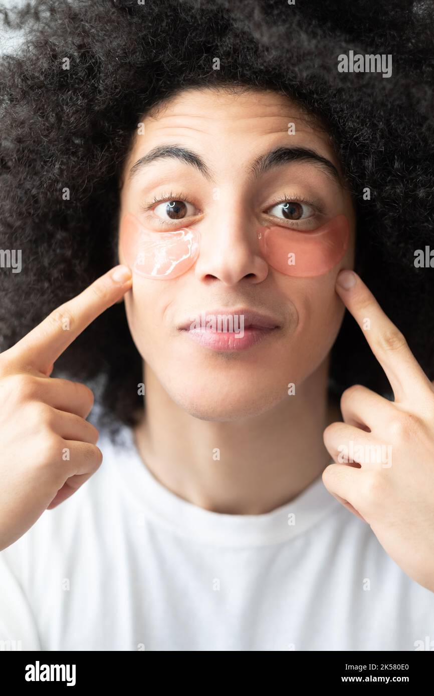 Soin du visage pour homme. Hydratant pour la peau. Produit cosmétique anti-âge. Surprise gars beau avec long brun cheveux bouclés montrant rose hydrogel yeux patchs o Banque D'Images Soin du visage pour homme. Hydratant pour la peau. Produit cosmétique anti-âge. Surprise gars beau avec long brun cheveux bouclés montrant rose hydrogel yeux patchs o Banque D'Images