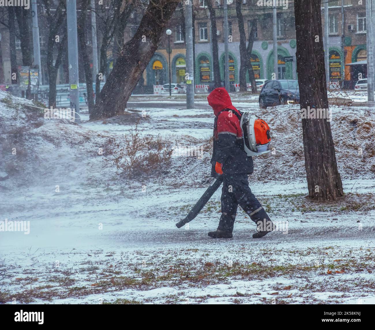 Travaux saisonniers des services publics de la ville dans le parc. Un travailleur équipé d'un souffleur de sac à dos motorisé souffle de la neige sur un sentier de parc. Banque D'Images
