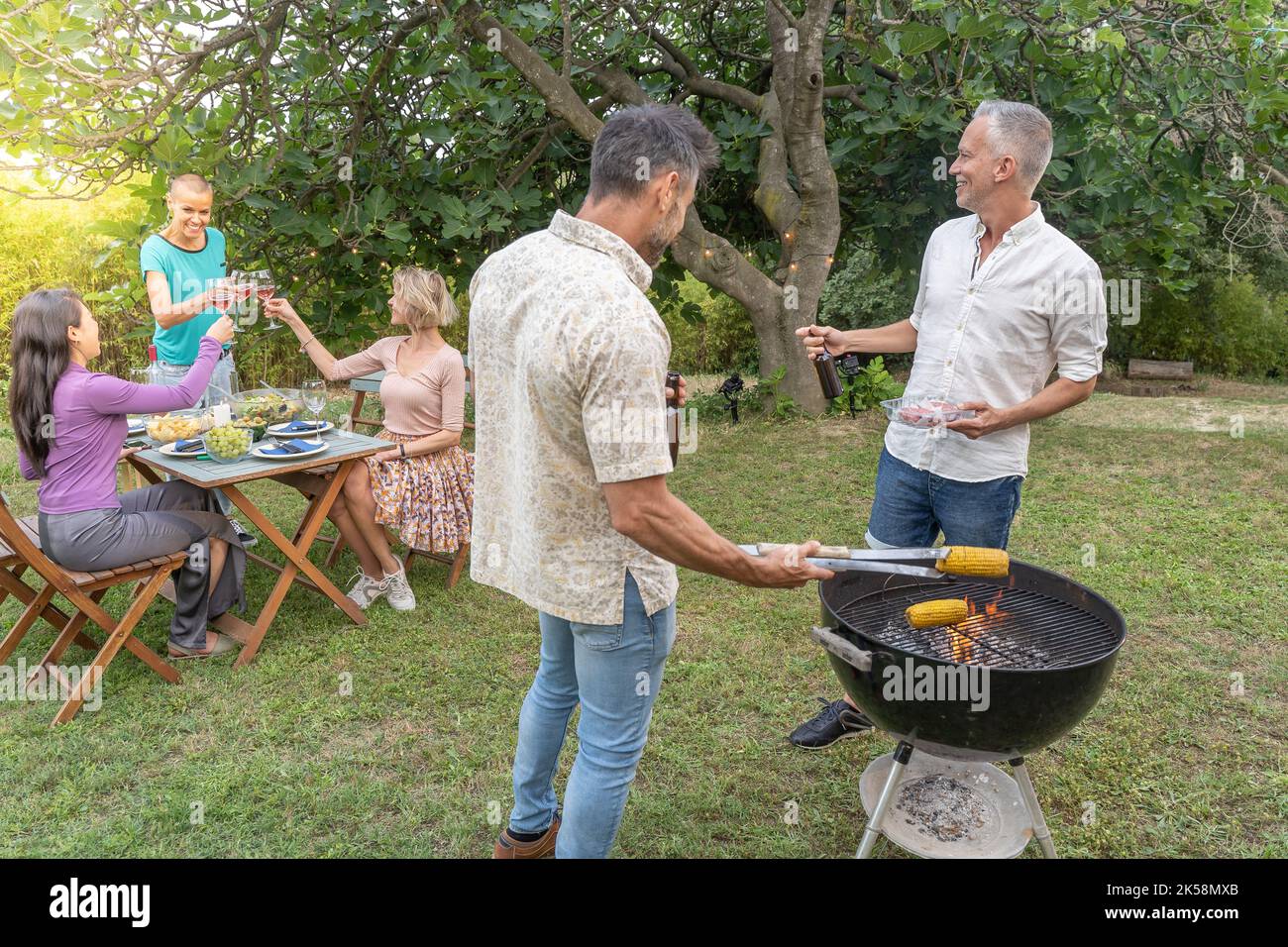 Amis cuisinant avec le barbecue avoir une conversation sourire heureux et rire ensemble parlant dans le patio. Banque D'Images