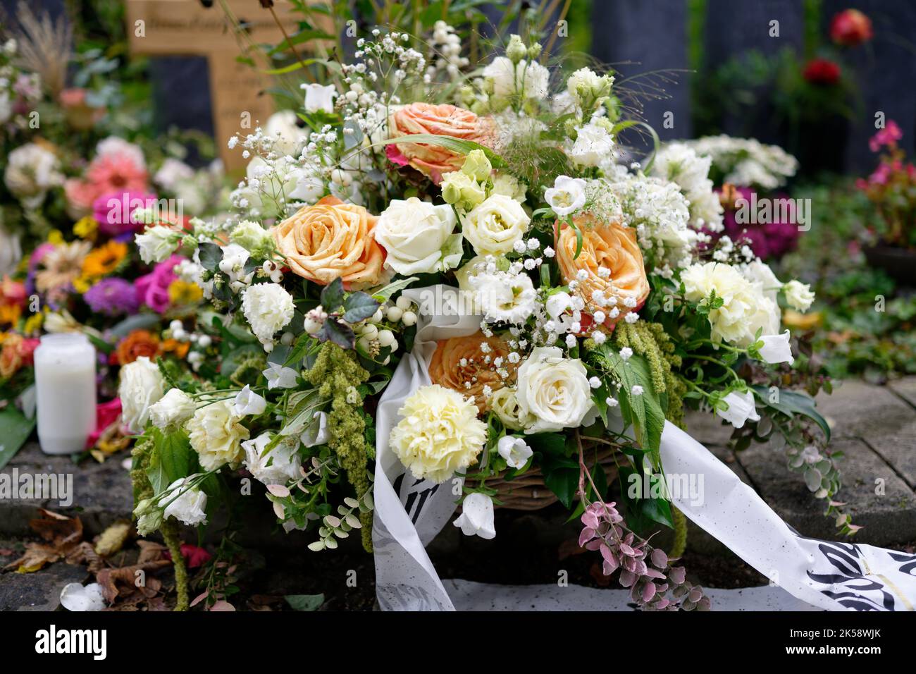 fleurs funéraires pastel sur une tombe devant une croix en bois sur fond flou Banque D'Images
