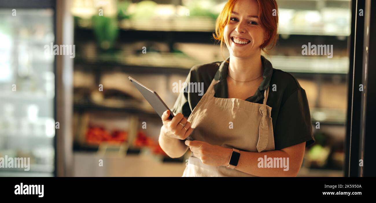 Un jeune propriétaire de boutique souriant à la caméra tout en tenant une tablette numérique. Joyeuse entrepreneur de la gestion d'une petite entreprise réussie dans le f Banque D'Images