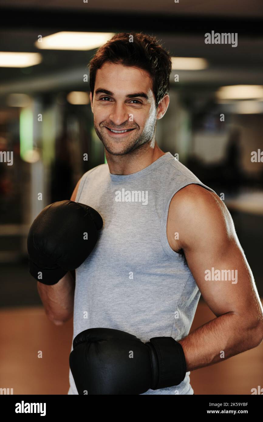 Prêt à l'emploi. Portrait d'un homme souriant portant des gants de boxe et des vêtements de sport se posant prêt à se battre à la salle de gym. Banque D'Images