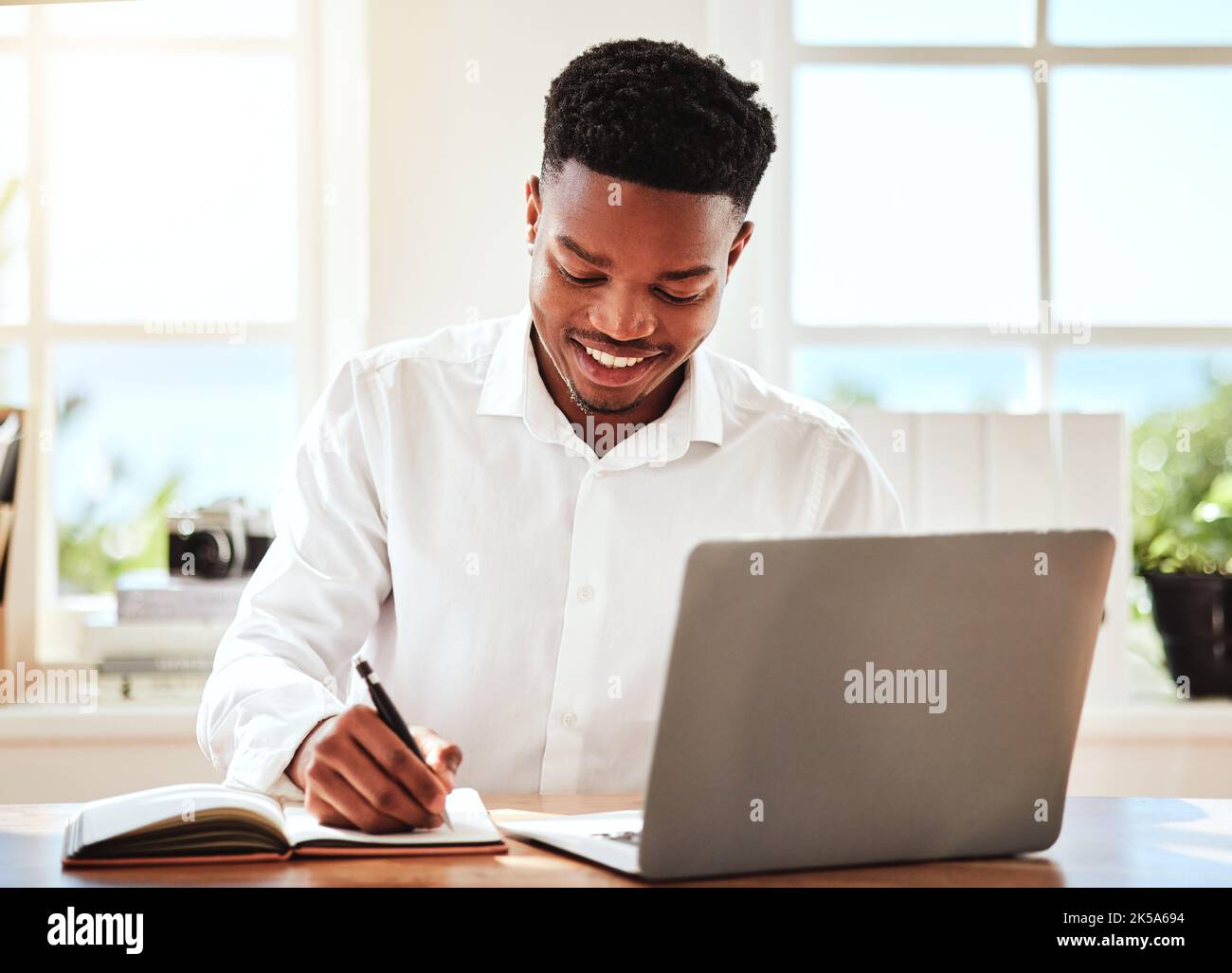 Internet, ordinateur portable et homme noir écrivant dans ordinateur portable, travailleur indépendant heureux. Homme d'affaires africain souriant faisant des recherches en ligne, prenant des notes pour Banque D'Images