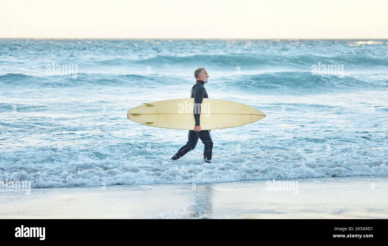Surf, vagues et surfeur homme marchant sur une plage avec une planche pour l'exercice et la remise en forme aquatique. Entraînement, entraînement et activité sportive d'un athlète sportif Banque D'Images