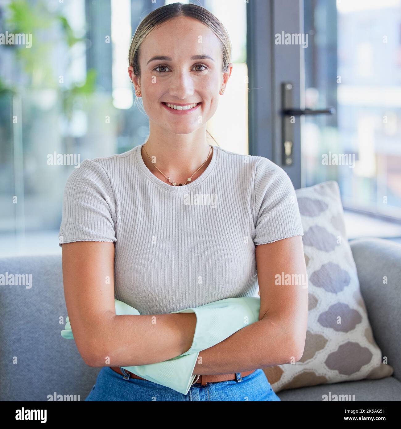 Portrait de femme de ménage avec des gants dans la salle de séjour heureux, sourire et satisfait après l'entretien intérieur de la maison. Service de nettoyage, bras croisés Banque D'Images