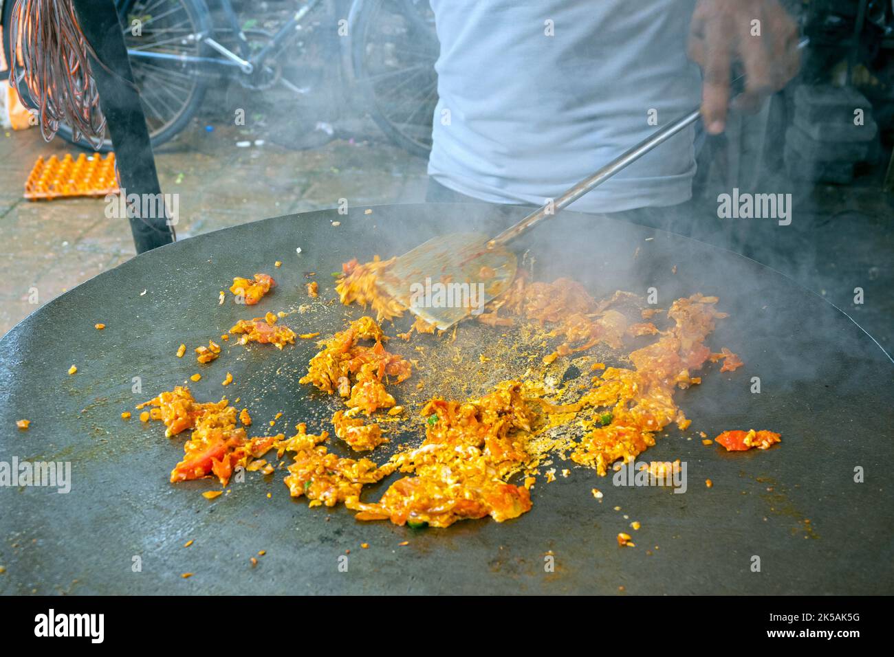 Personne cuisant une omelette épicée traditionnelle sur une poêle à frire chaude dans le marché de rue asiatique, Inde Banque D'Images