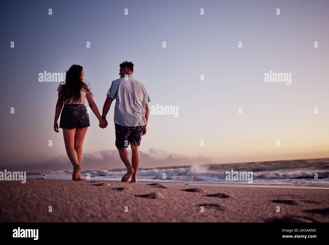 Couple, tenant les mains et l'amour pour la promenade de plage ensemble dans le coucher de soleil romantique d'été en plein air. Main de l'homme et de la femme marchant sur un beau Banque D'Images
