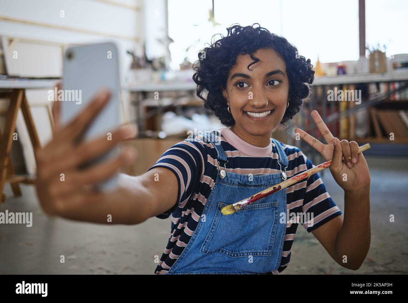 Artiste indienne, selfie avec pinceau et art au sol de l'atelier de studio à partager sur les médias sociaux. Portrait d'un professionnel joyeux et créatif Banque D'Images