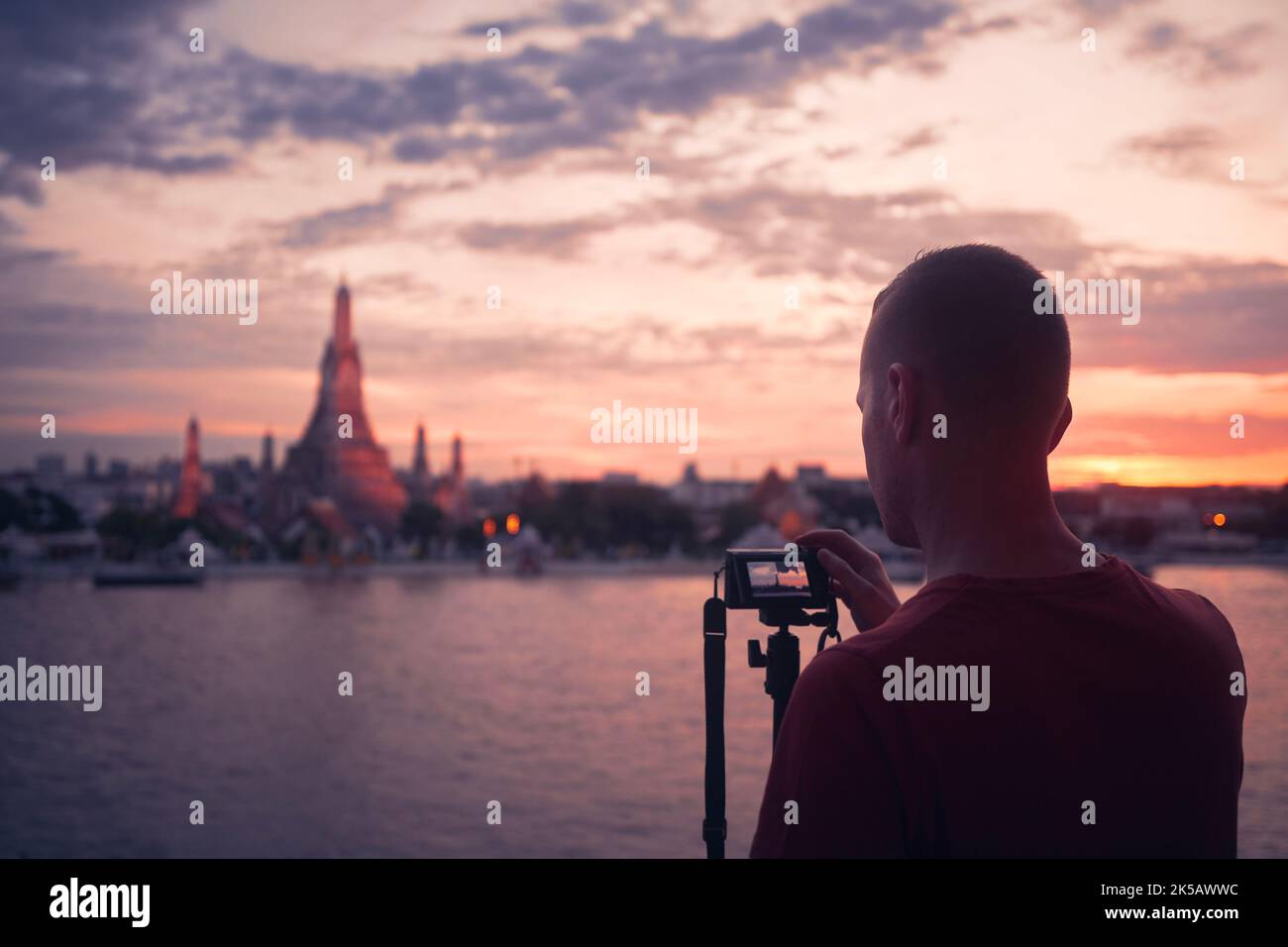 Homme photographiant le paysage urbain au coucher du soleil. Tourisme avec appareil photo sur trépied contre le temple de Wat Arun à Bangkok, Thaïlande. Banque D'Images