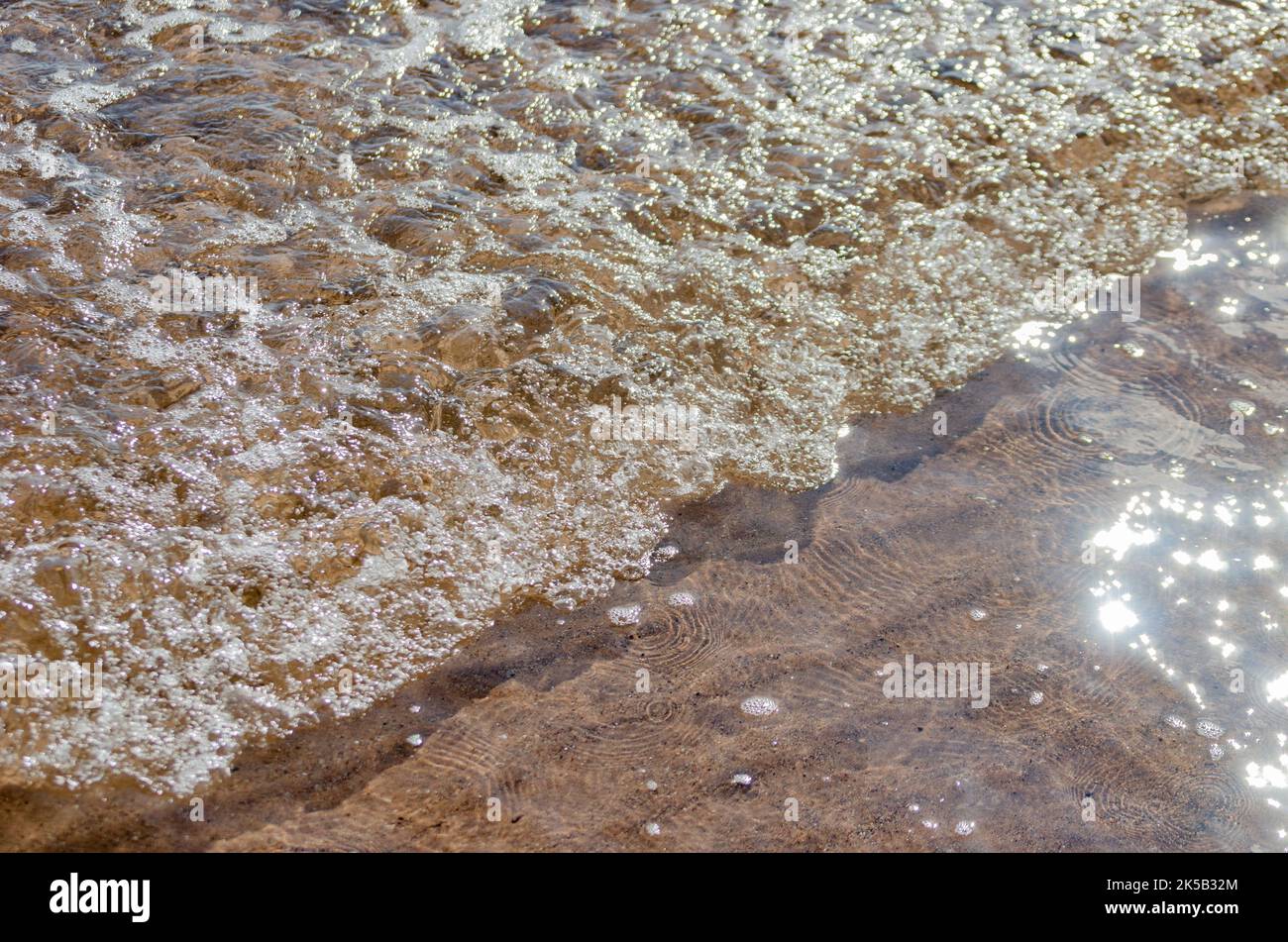 Petites vagues bouillonnantes se brisant dans les eaux peu profondes de la plage en plein soleil avec flou de mouvement et fond de mise au point sélective Banque D'Images