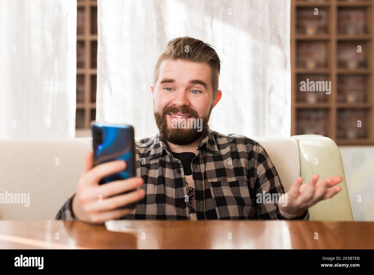Happy young man sitting at coffee tourné avec vos écouteurs faisant appel vidéo à un ami. Homme de race blanche ayant video chat sur smart phone at cafe. Banque D'Images