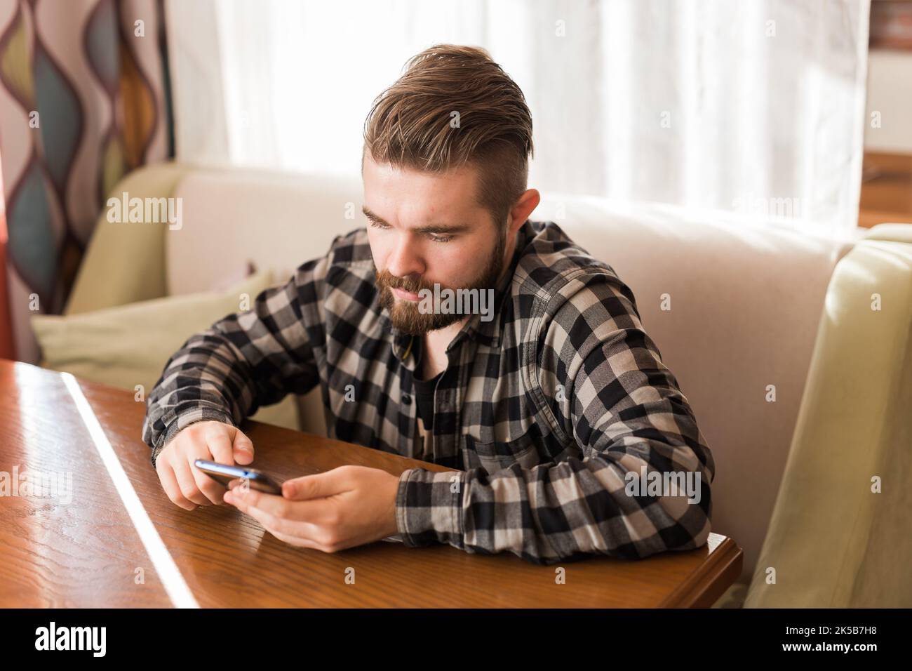 Jeune homme hippster à la recherche de nouvelles des réseaux sociaux lus via smartphone sur le temps libre dans le café Banque D'Images