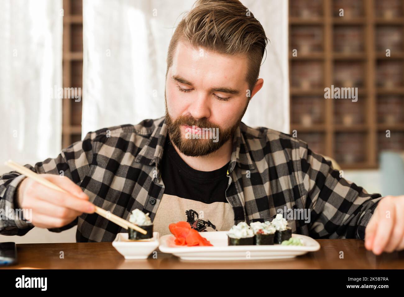Homme mangeant des petits pains à sushis dans un restaurant. Guy mangeant de la cuisine japonaise à l'aide de bâtonnets de bambou. Culture, alimentation et tradition dans le monde moderne Banque D'Images