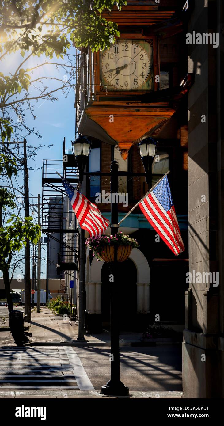 Le soleil du matin brille sur les drapeaux en dessous d'une grande horloge dans le quartier du centre-ville de Manitowoc, Wisconsin. Banque D'Images