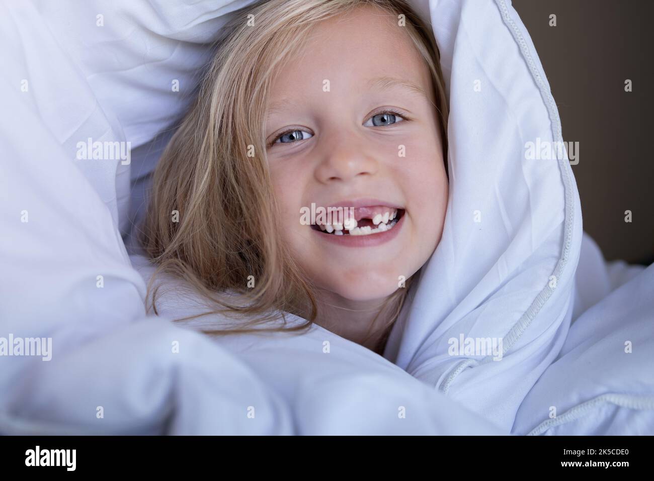 petite fille sans dents de devant souriant le matin au lit Banque D'Images